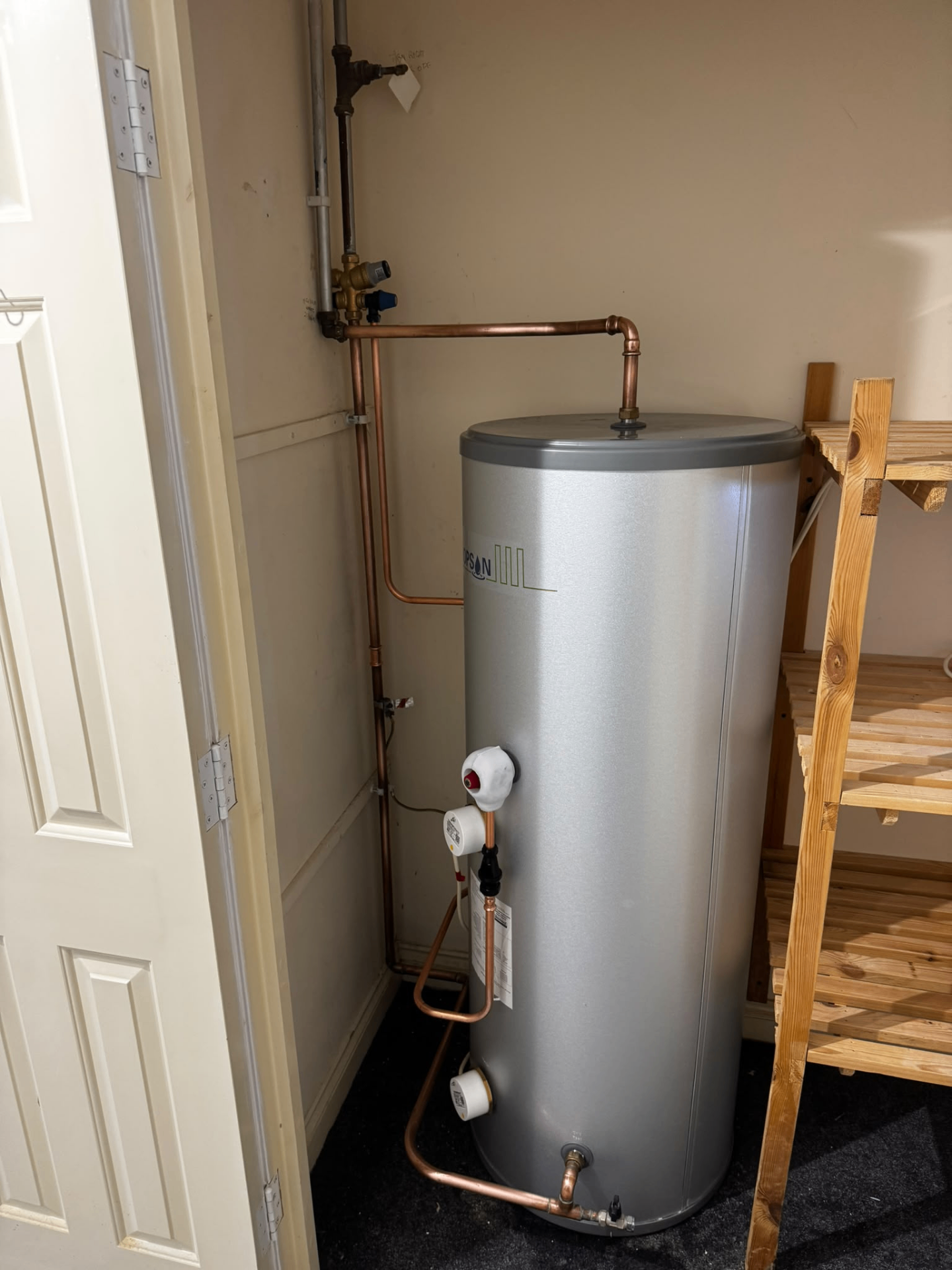 Stainless hot water cylinder installation in a storage room with neatly routed copper connections
